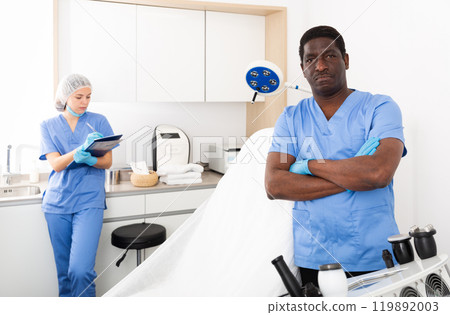 Confident cosmetologist in aesthetic medicine office with female assistant 119892003