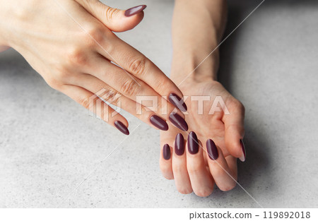 Elegant hands with almond-shaped maroon nails displayed against a gray tabletop 119892018