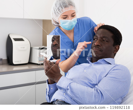 Woman beautician in mask examining face skin of afro american male patient Woman beautician in mask examining face skin of afro american male patient 119892118