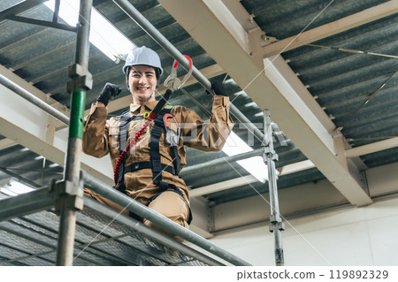 一名工人爬上建築工地的鷹架，用拳頭打氣筒 119892329