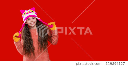 Winter fashion style. Teenager knitted fashion. Outdoor lifestyle fashion. Teenager girl in a winter warm hat isolated on red. Happy girl in winter hat. Copy space banner 119894127