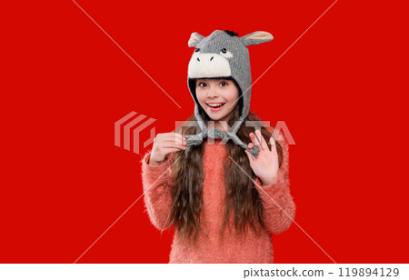 Teenager girl in a winter warm hat isolated on red. Happy girl in winter hat. Winter fashion style. Childhood development. Teenager knitted fashion. Outdoor lifestyle fashion 119894129