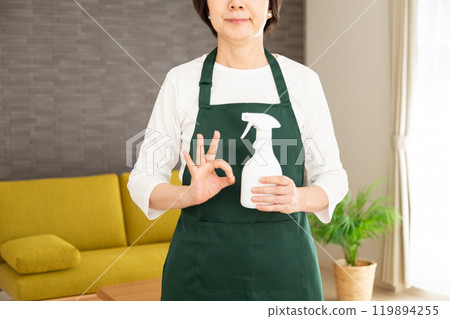 一位身穿綠色圍裙的高級女家庭主婦/管家在她家的客廳裡做一個圓圈標誌 119894255