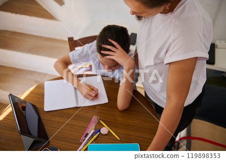 Parent helping child with homework at a wooden table 119898353
