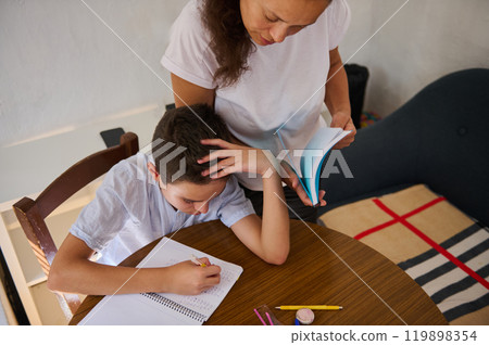 Mother assisting son with homework at wooden table Mother assisting son with homework at wooden table 119898354
