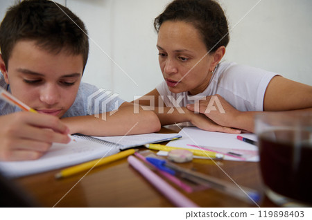Mother helps her son with homework at the kitchen table 119898403
