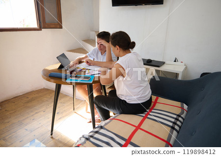 Two women collaborating at home with a laptop and documents 119898412