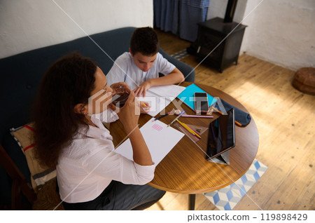 Mother and child studying together at wooden table with tablet Mother and child studying together at wooden table with tablet 119898429