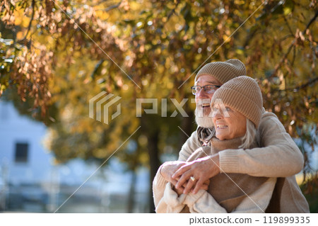 Portrait of beautiful senior couple during walk in autumn park. Elderly husband and wife are embracing each other. 119899335