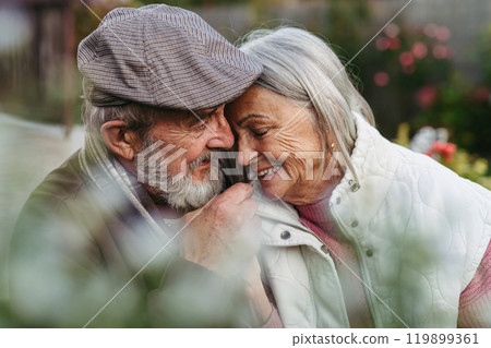 Portrait of beautiful senior couple outdoors in an autumn garden. Elderly husband and wife are embracing each other. Portrait of beautiful senior couple outdoors in an autumn garden. Elderly husband and wife are embracing each other. 119899361