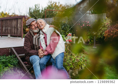 Portrait of beautiful senior couple outdoors in an autumn garden. Elderly husband and wife are embracing each other. 119899362