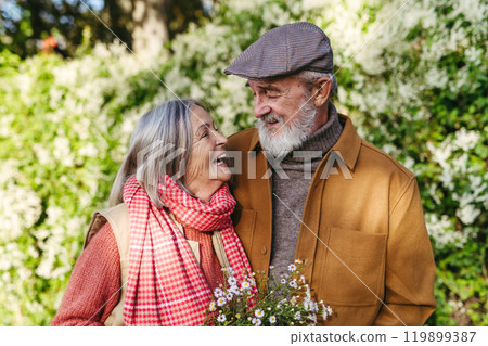 Portrait of beautiful senior couple outdoors in an autumn garden. Elderly husband and wife looking at each other lovingly. 119899387
