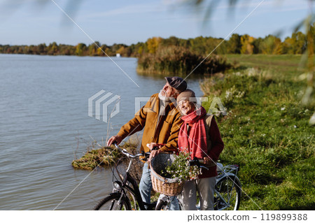 Lovely elderly couple on standing by lake with their bikes, enjoying a peaceful moment together. 119899388