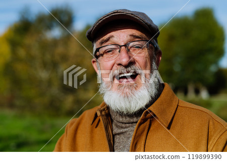 Portrait of friendly older man with a gray beard. Senior standing outdoors in nature, looking at camera and smiling. 119899390
