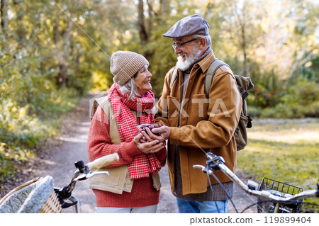 Lovely elderly couple on standing in the middle of autumn nature with their bikes, foraging for chestnuts. 119899404