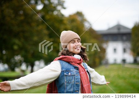 Portrait of a beautiful woman in the middle of autumn park, standing with outstretched arms, enjoying seasonal weather around her. Portrait of a beautiful woman in the middle of autumn park, standing with outstretched arms, enjoying seasonal weather around her. 119899414