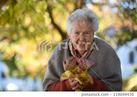 Portrait of elderly woman on walk in the park during warm autumn day, holding handful of colorful leaves. Portrait of elderly woman on walk in the park during warm autumn day, holding handful of colorful leaves. 119899430