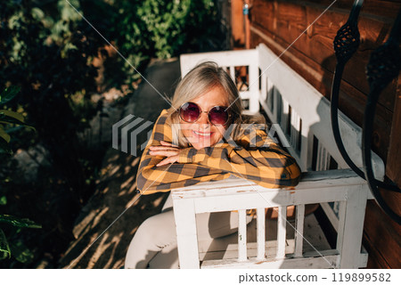 Beautiful older women is sitting in front of her cabin, enjoying autumn sun rays on her face. 119899582