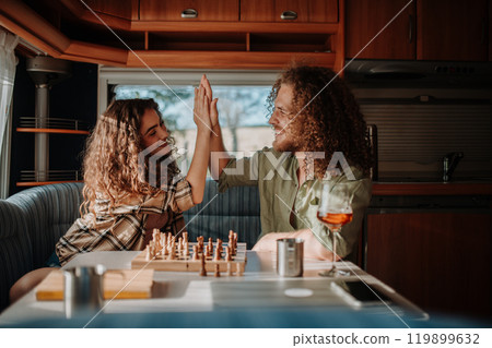 Young couple is on a camping trip in nature, sitting in caravan and playing chess. Caravan traveling for young people. 119899632