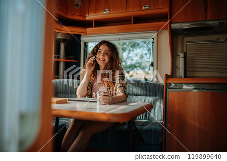 Young beautiful woman is on a camping trip in nature, sitting in her caravan making phone call. Caravan as homeoffice, working remotely. 119899640