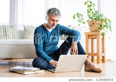 Homeoffice for handsome man. Man sitting on floor and working on laptop with headphones on head. Telecommuting. Homeoffice for handsome man. Man sitting on floor and working on laptop with headphones on head. Telecommuting. 119899703