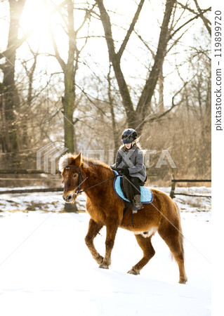 Young girl spending cold winter weekend on family farm, riding her brown fluffy pony through snowy countryside. Young girl spending cold winter weekend on family farm, riding her brown fluffy pony through snowy countryside. 119899720