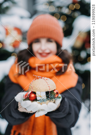 Woman in warm orange winter wear holding a festive holiday treat. Christmas market experience, cozy outdoor snacks, seasonal trends in holiday street food and decor 119899928