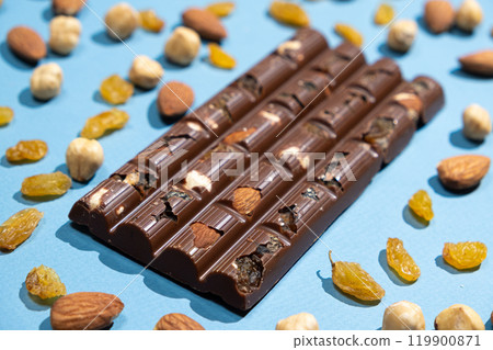 Nutty milk chocolate among scattered almonds, raisins and hazelnuts. 119900871