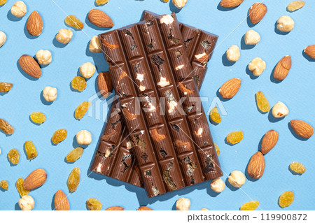 Nutty chocolate bars among scattered nuts and raisins on a blue background. 119900872