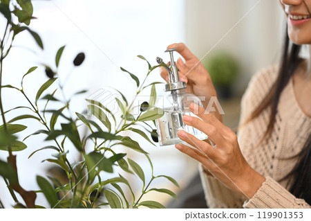 Young woman examining a potted plant in a living room. Home gardening and mindfulness concept 119901353