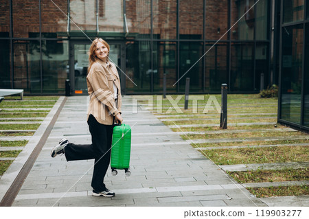 Cheerful young woman in casual outfit walking on the city park with green luggage. 30s Woman dragging suitcase near hotel. Travel Fashion concept. Full body Cheerful young woman in casual outfit walking on the city park with green luggage. 30s Woman dragging suitcase near hotel. Travel Fashion concept. Full body 119903277
