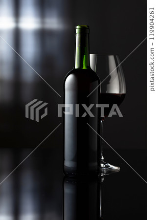 Glass and bottle of red wine on a black reflective background. 119904261