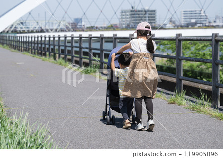 A cute older sister takes care of her younger child who is pushing a stroller on the riverbank A cute older sister takes care of her younger child who is pushing a stroller on the riverbank 119905096