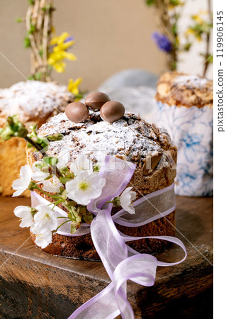 Homemade Italian traditional Easter panettone cake, decorated by chocolate eggs, pink ribbon and blossoming cherry tree flowers standing on wooden table. Traditional Easter European bake. Close up 119906145