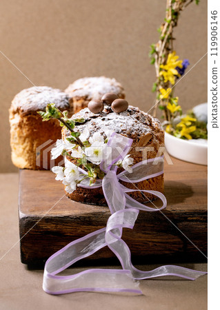 Homemade Italian traditional Easter panettone cakes, decorated by chocolate eggs, pink ribbon and blossoming cherry tree flowers standing on wooden table. Traditional Easter European bake. Homemade Italian traditional Easter panettone cakes, decorated by chocolate eggs, pink ribbon and blossoming cherry tree flowers standing on wooden table. Traditional Easter European bake. 119906146