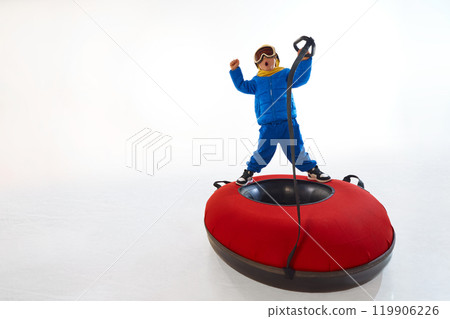 Little boy in blue winter suit and yellow beanie crouches atop red snow tube, ready for thrilling ride. Excitement of winter activities. 119906226