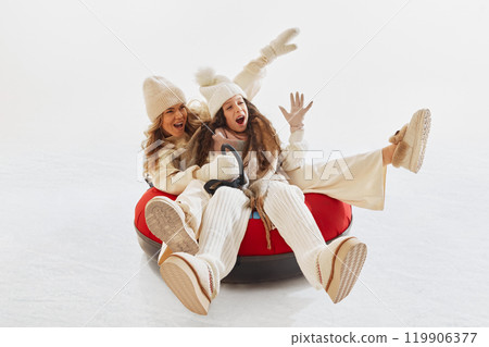 Joyful moment as mother and daughter laughing together while riding snow tube. Woman and girl dressed in cozy winter clothes 119906377