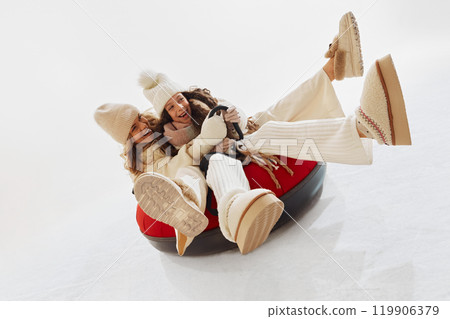 Joyful moment as mother and daughter laughing together while riding snow tube. Woman and girl dressed in cozy winter clothes Joyful moment as mother and daughter laughing together while riding snow tube. Woman and girl dressed in cozy winter clothes 119906379