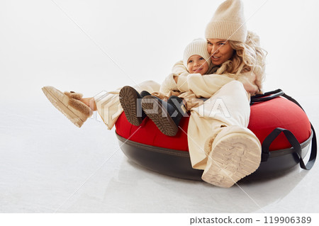 Mother and her young son enjoying exciting ride on red snow tube. Both wearing cozy winter attire, having fun during outdoor winter activities. 119906389