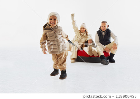Happy family dressed in winter clothes enjoying time on snow, with little boy pulling tube. Winter outdoor fun and bonding. 119906453