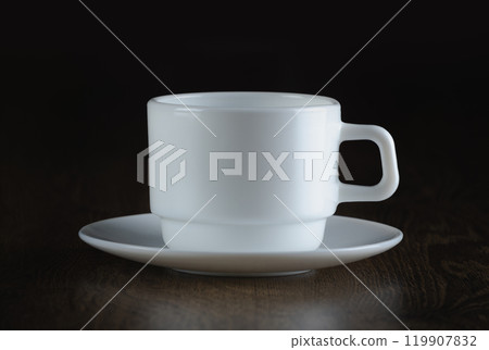 An empty white cup and saucer rest on a dark wooden surface An empty white cup and saucer rest on a dark wooden surface 119907832
