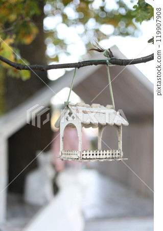 Bird feeder hanging on a tree, birdbox in shape of a little house. Birdhouse made out of wood in white  119907908