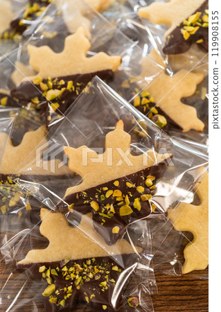 Carefully packaging Christmas cutout cookies, half-dipped in chocolate and presented in clear cellophane wrapping, perfect for festive gifting. 119908155