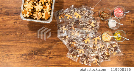 Carefully packaging Christmas cutout cookies, half-dipped in chocolate and presented in clear cellophane wrapping, perfect for festive gifting. Carefully packaging Christmas cutout cookies, half-dipped in chocolate and presented in clear cellophane wrapping, perfect for festive gifting. 119908156