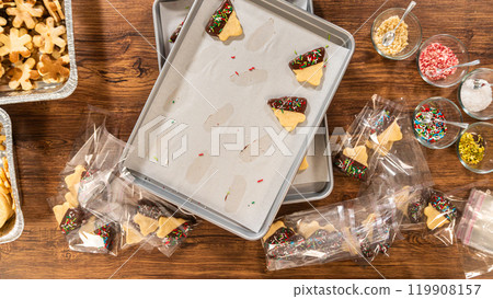 Carefully packaging Christmas cutout cookies, half-dipped in chocolate and presented in clear cellophane wrapping, perfect for festive gifting. Carefully packaging Christmas cutout cookies, half-dipped in chocolate and presented in clear cellophane wrapping, perfect for festive gifting. 119908157