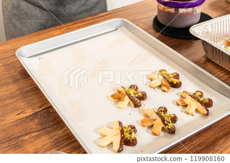 Crafting star-shaped holiday cookies dipped in chocolate and sprinkled with crushed pistachios, arranged on parchment paper. Crafting star-shaped holiday cookies dipped in chocolate and sprinkled with crushed pistachios, arranged on parchment paper. 119908160