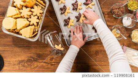 Preparing star-shaped cookies, half-dipped in chocolate, accented with peppermint chocolate chips for the holidays. 119908161