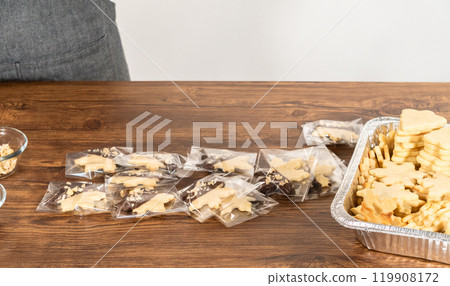 Carefully packaging Christmas cutout cookies, half-dipped in chocolate and presented in clear cellophane wrapping, perfect for festive gifting. 119908172