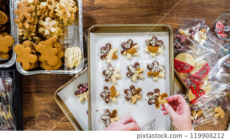 Flat lay. Carefully packaging Christmas cutout cookies, half-dipped in chocolate, sprinkled with crushed nuts, and presented in clear cellophane wrapping. 119908212