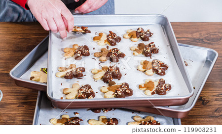 Carefully packaging Christmas cutout cookies, half-dipped in chocolate and presented in clear cellophane wrapping, perfect for festive gifting. 119908231